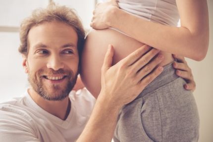 Mann hört an Bauch einer schwangeren Frau